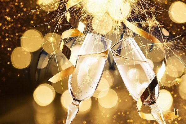 Zwei Champagnergläser stoßen inmitten von goldenem Licht und festlichem Funkeln an.