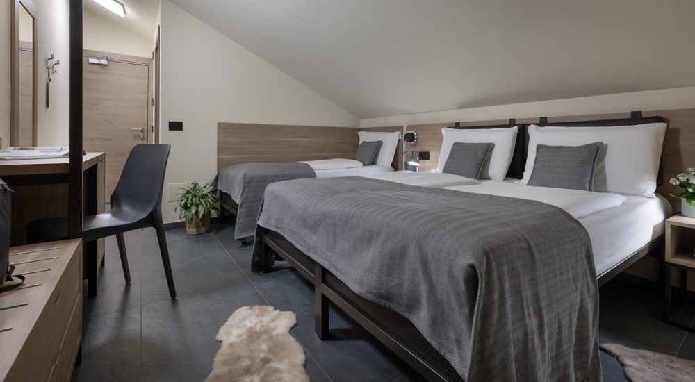 Modernes Hotelzimmer mit drei Einzelbetten, Holzmöbeln und minimalistischer Einrichtung.