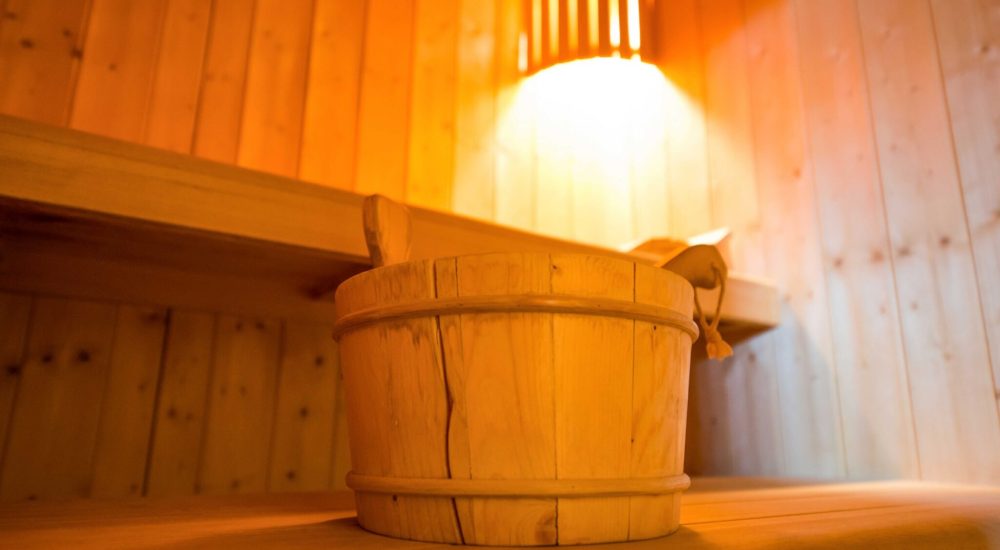 Ein Holzeimer auf einer Bank in einer von warmem Licht erhellten Sauna.