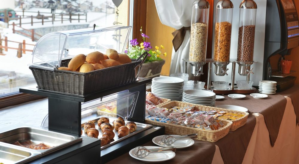 Frühstücksbuffet mit Brot, Croissants und Müsli neben einem verschneiten Fenster.