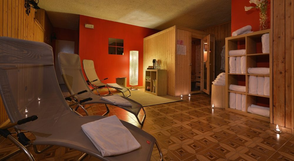 Entspannungsbereich eines Spas mit Liegen, Handtüchern und einer Sauna aus Holz.