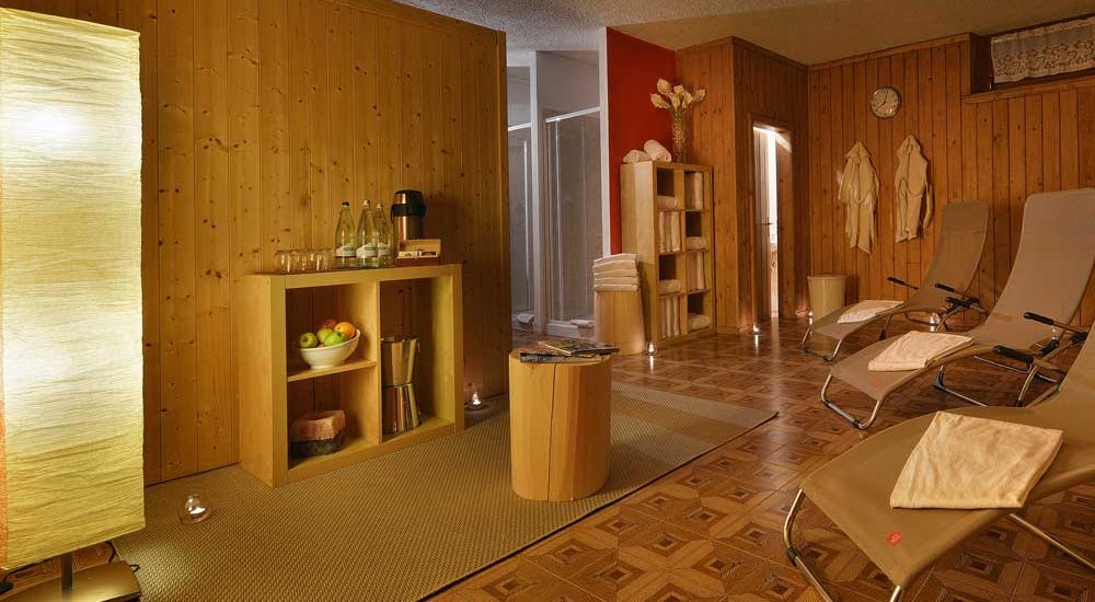Entspannungsraum eines Spas mit Liegen, aufgehängten Bademänteln und Getränken auf einem Holzregal.